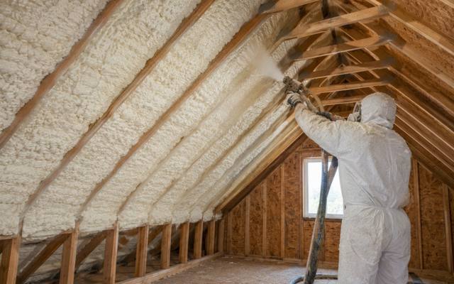 Installer spraying foam between attic rafters